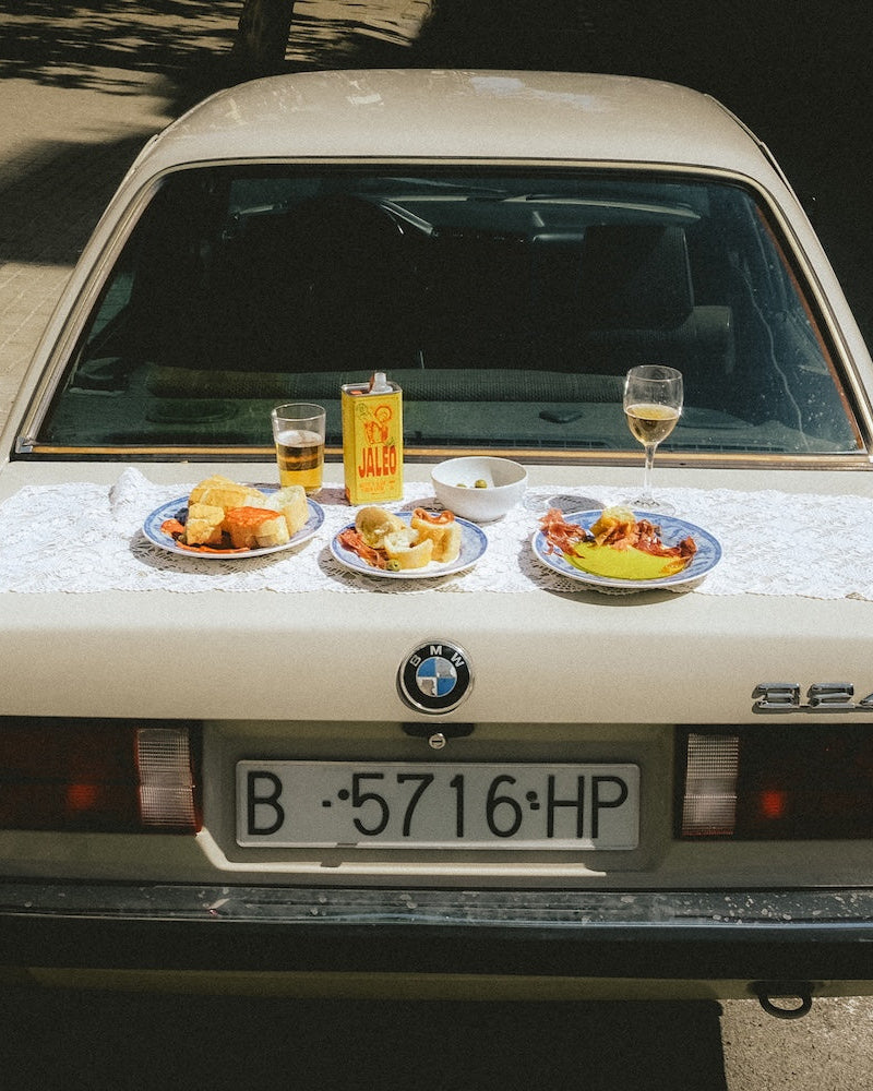 Lata de Jaleo Del Bueno sobre el maletero de un coche, entre platos de aperitivo y un vaso de vino